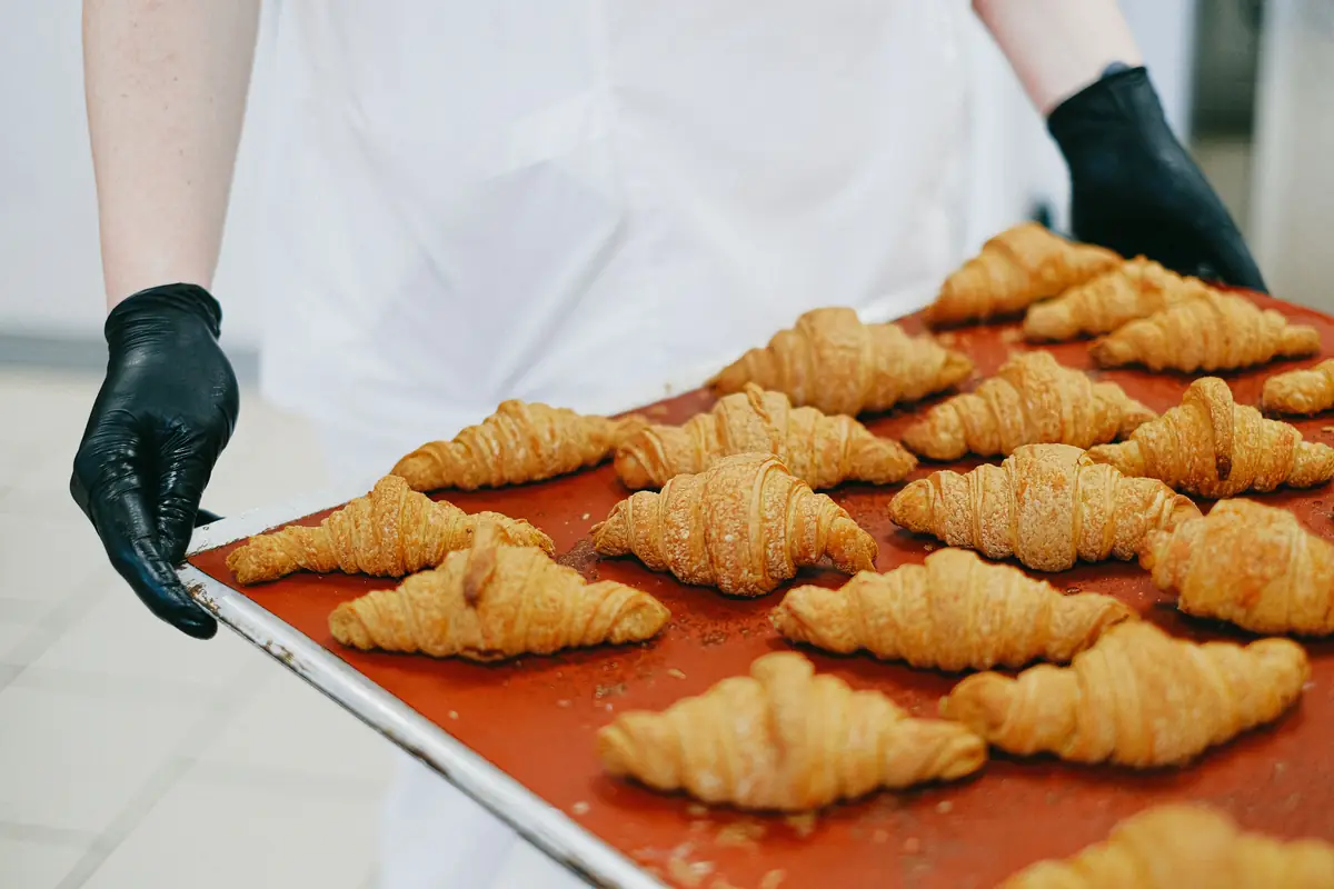 A baker holding a tray of unbaked croissants in a production kitchen