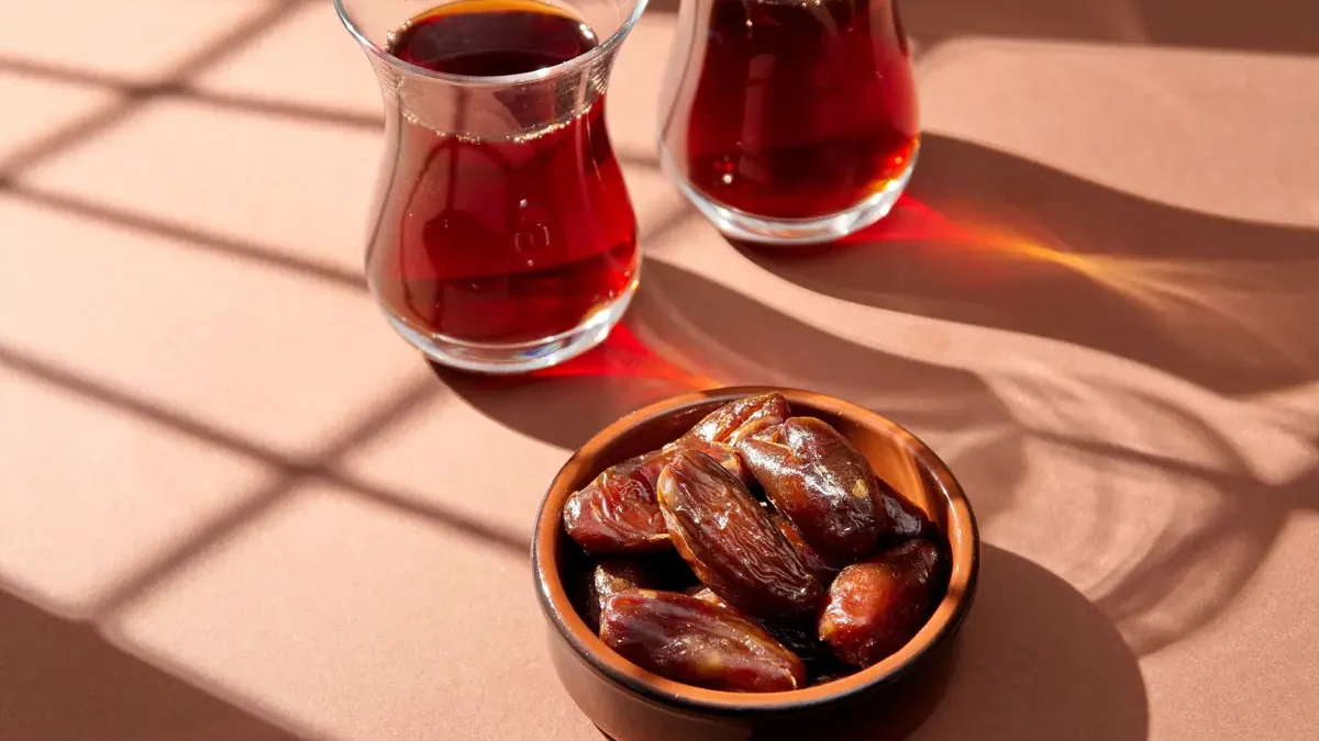 Dark date syrup served in glasses beside a bowl of dates