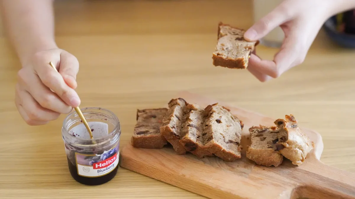 A jar of dark date jam with a wooden spoon and bread