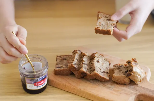 A jar of dark date jam with a wooden spoon and bread
