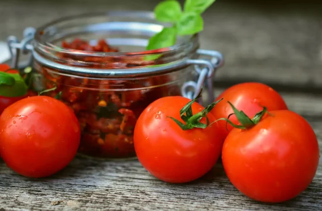 A jar of sun-dried tomatoes in oil beside fresh tomatoes